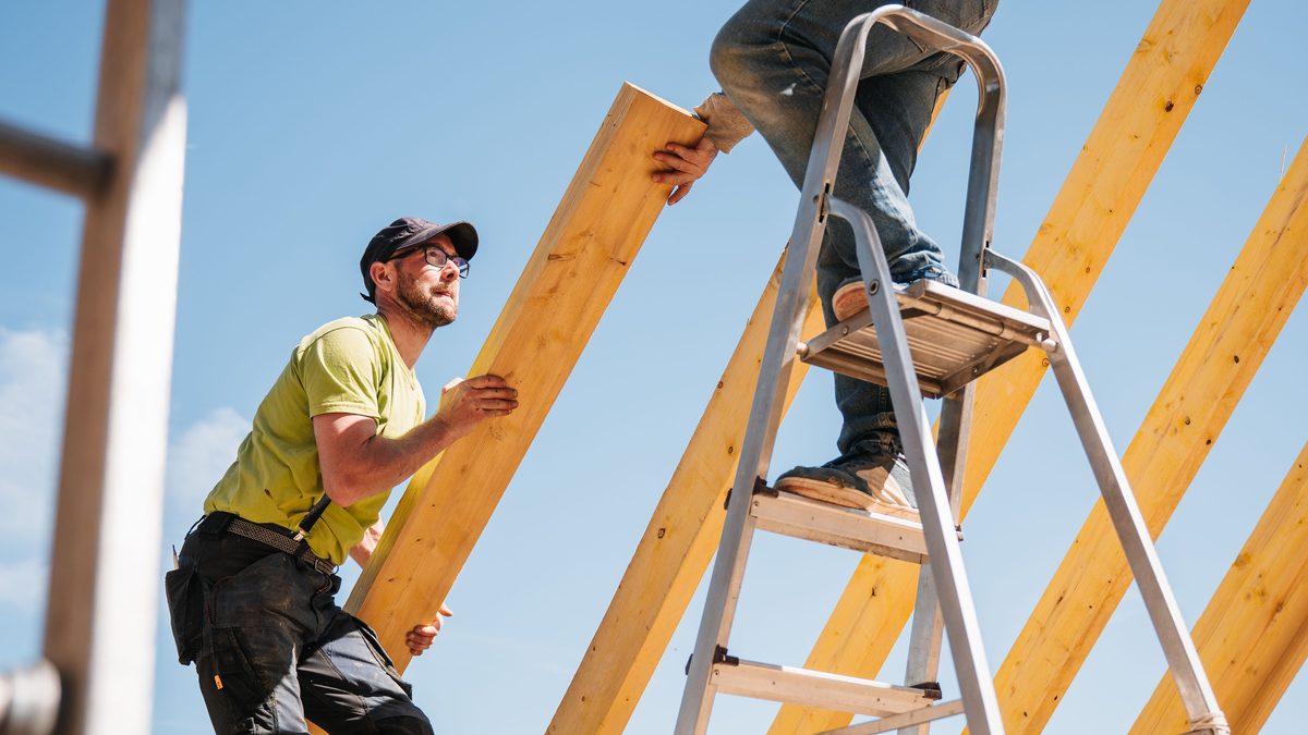 Roofing crew framing a new roof structure with wooden rafters against a blue sky